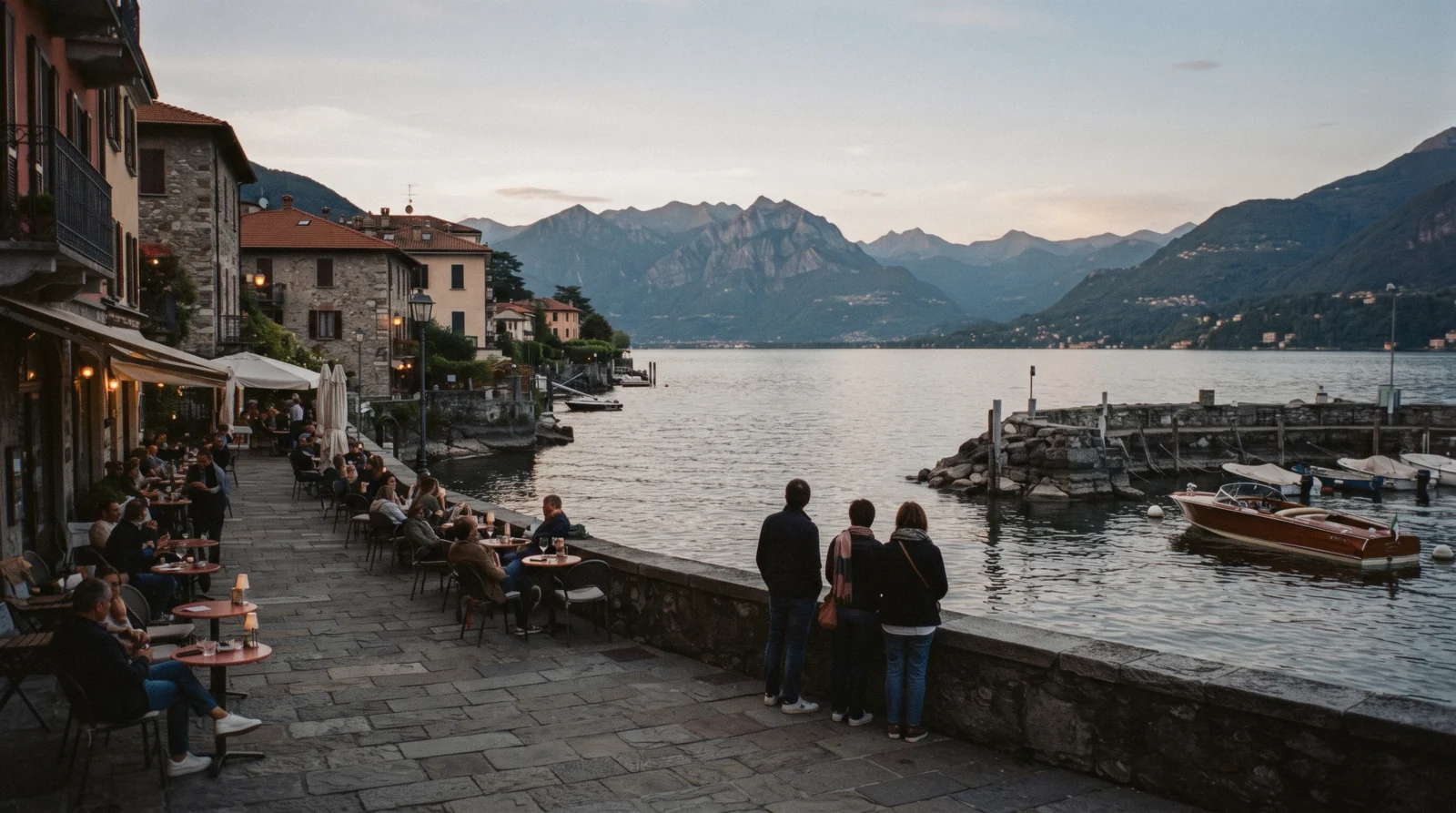 The waterfront square and moored boats at Cernobbio on Lake Como, with the wooded ridge above the town catching late light