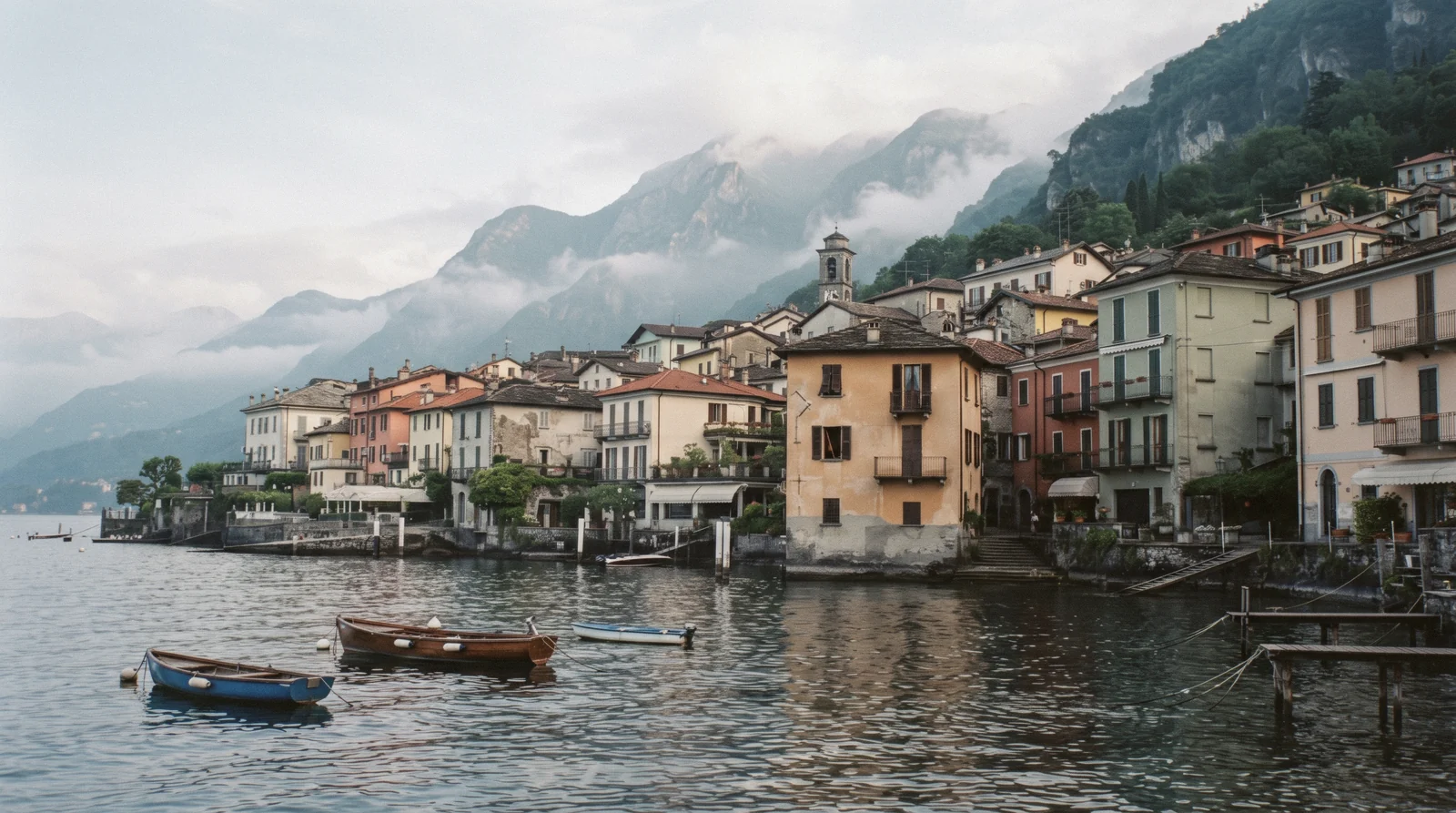 Pastel waterfront houses and a landing stage on the centre of the lake, one of the Lake Como towns a visitor chooses between